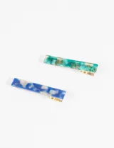 Set de dos clips rectangulares para el pelo, uno con diseño acrílico en tonos azules y blancos, y otro con diseño acrílico en tonos verdes y dorados.
