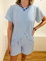 Conjunto de dos piezas color celeste claro, compuesto por un remerón de manga corta con diseño cruzado envolvente en la parte delantera y un short liso a juego.