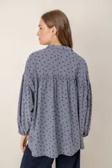 Camisa de corte oversize y diseño holgado, color celeste con estampado de pequeños corazones negros. Presenta cuello clásico, cierre frontal con botones y mangas largas abullonadas con puños ajustados.