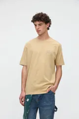 Remera de manga corta color beige, confeccionada en jersey de algodón con textura suave y calce relaxed. Presenta costuras a contratono en la espalda y un diseño estampado en la parte posterior con ilustraciones de estilo lineal y frases manuscritas.