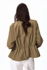 Campera en sarga de algodón color beige, con cuello, cierre frontal con botones ocultos y cordón ajustable en la cintura. Presenta bolsillos de parche con solapa en el pecho y mangas largas.