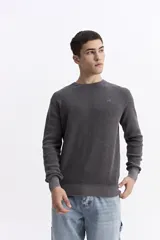 Sweater de hombre con textura waffle, color verde oliva desgastado (acid wash), cuello redondo y puños y ruedo acanalados. Presenta un pequeño logo bordado en el pecho.