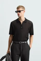 Polo de manga corta color negro, con cuello solapa y cierre frontal de botones. Confeccionado en tejido de punto con estructura abierta y calada.