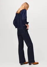 Camisa de jean de algodón con cuello camisero, cierre frontal de botones ocultos, mangas largas con puños abotonados y dos bolsillos delanteros con solapa.