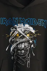 Canguro negro de corte oversized con capucha, bolsillo frontal tipo canguro y estampado frontal de la banda Iron Maiden con diseño de momia. Las mangas presentan detalles estampados en color dorado con motivos egipcios.