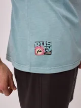 Remera holgada de algodón color beige, de manga corta y cuello redondo, con un gran estampado colorido en la espalda con diseño de olas y la inscripción 'Rusty Tribe'.