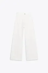 Pantalón de jean blanco de tiro alto y corte wide leg, con bolsillos delanteros y traseros. Cierre frontal con cremallera y botón metálico.