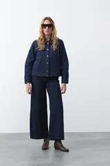 Campera de jean color negro con cuello de pana en tono marrón, cierre frontal con botones metálicos y bolsillos frontales tipo cargo.