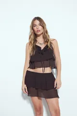 Falda corta de color marrón oscuro, con cintura lisa y volados escalonados superpuestos que le dan textura y movimiento.