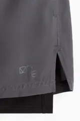 Short deportivo gris con calza interior negra, corte estándar, con cintura elástica y cordón ajustable.