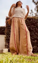 Pantalón ancho de lino color tostado, con cintura elástica y detalles de bordado rojo a lo largo de las piernas.