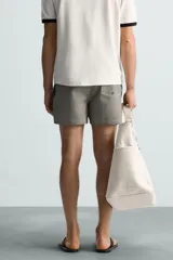 Bañador de hombre color verde claro con finas rayas blancas verticales (efecto seersucker). Tiene cintura elástica ajustable con cordón verde, bolsillos laterales y un bolsillo trasero de vivo.