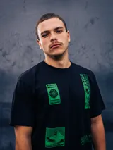 Remera negra de manga corta, corte holgado, con cuello redondo y estampado frontal en color verde con gráficos y texto de estilo japonés.