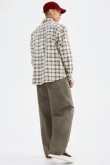 Camisa de manga larga con cuello inglés, tapeta clásica y canesú en la espalda. Presenta un bolsillo superior abierto y bajo redondeado. El tejido es suave de algodón con un patrón de cuadros en tonos celeste, marrón y beige.