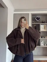 Campera tipo bomber de corte oversize y diseño holgado, confeccionada en gamuza color marrón. Presenta cierre frontal, cuello camisero y hombreras con detalle de trabas.