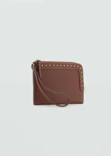 Funda de poliuretano efecto piel color marrón, con detalle de tachuelas metálicas doradas, cierre de cremallera y asa corta de mano.