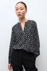 Blusa negra con estampado de lunares blancos, escote en V y mangas largas con puños abotonados.