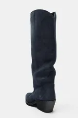 Bota alta de estilo cowboy confeccionada en serraje de color azul marino, con tacón medio en bloque y puntera perfilada. Presenta costuras decorativas en el cuerpo y diseño de calce fácil.