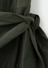 Vestido midi evasé color verde oscuro, sin mangas con tirantes anchos, cuello redondo y detalle de pañuelo cruzado en la cintura con lazo lateral. Cuenta con cierre de cremallera lateral.