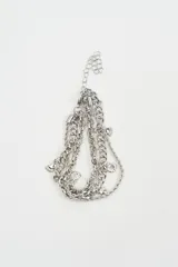 Brazalete multicapa de color plateado compuesto por cadenas de diferentes texturas y eslabones, con dijes colgantes en forma de conchas marinas y pies.