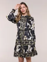 Vestido corto de satén estampado en tonos negro y beige con diseño floral y geométrico, cuello camisero con solapa, mangas largas con puños, lazo ajustable en la cintura y falda con volado en el ruedo.