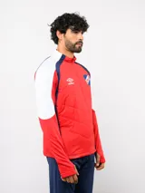 Buzo de entrenamiento Umbro del Club Nacional de Football, con cierre frontal parcial y cuello alto. Presenta un diseño con bloques de color azul, blanco y rojo, con panel frontal acolchado y mangas largas con aberturas para pulgares.