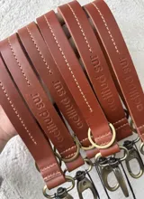 Llavero de cuero en formato de tira con diseño minimalista, confeccionado en cuero genuino marrón con interior en contraste color fucsia, pespuntes rosados y herrajes metálicos envejecidos con gancho tipo mosquetón.