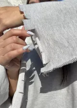 Buzo oversize de color gris, con diseño de costuras expuestas en contraste y terminaciones desflecadas en mangas y ruedo.