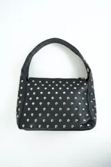 Cartera de hombro color negro, confeccionada en material sintético con textura graneada, totalmente decorada con tachas metálicas plateadas y cierre superior.
