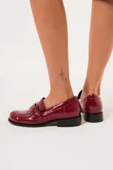 Mocasines color rojo charol con hebilla metálica y ojalillos.