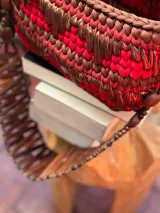 Bolso de mano tejido a mano con tiras de material orgánico en tonos tierra (rojo, marrón, beige) sobre una base de eco-cuero. Posee un asa de mano hecha de un cinturón vintage.