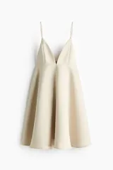 Vestido corto color beige, con escote en V pronunciado, tirantes finos ajustables, corte bajo el busto y falda acampanada con vuelo.