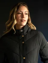 Campera negra acolchada con capucha con borde de piel sintética negra desmontable, cierre frontal con cremallera y botones a presión dorados, bolsillos laterales y puños elásticos.