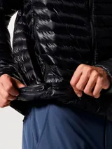 Campera puffer ultraligera Mountain Hardwear, modelo Ghost Whisperer, color negro. Confeccionada en tejido ripstop reciclado con aislamiento de plumón de 800 hilos. Cuenta con capucha, cierre frontal completo, dos bolsillos laterales con cremallera y diseño altamente compactable.