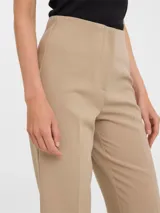 Pantalón de vestir color beige claro, tiro alto, corte recto y largo al tobillo. Presenta pinzas frontales y un acabado liso y elástico.