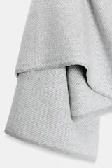 Abrigo corto tipo capa confeccionado en lana, con diseño de cuello envolvente tipo bufanda y mangas anchas. Presenta una textura sutilmente jaspeada y cierre frontal oculto.