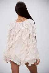 Blusa color crudo con volados en el frente y en las mangas largas, confeccionada en tela semitransparente con cierre frontal de botones.