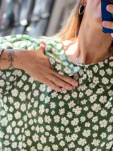 Blusa de corte holgado con estampado floral en tonos verde y blanco. Presenta cuello redondo tipo bebé, mangas cortas abullonadas y cierre frontal con botones ocultos.