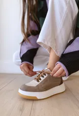 Championes de cuero color visón con cordones marrones, suela blanca y base color caramelo.