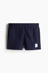 Short de baño de nylon azul marino con cintura elástica y cordón ajustable oculto, bolsillos laterales, bolsillo trasero con solapa y cierre autoadherente. Cuenta con suspensor interior de malla y un pequeño parche estampado en la pierna izquierda.