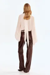 Blusa oversized de tejido liviano con efecto arrugado, cuello elevado drapeado con abertura en V, frunces frontales y tiras largas en la espalda. Presenta mangas globo largas de corte raglán con costura interior abierta y puños elásticos.