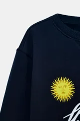 Sudadera de cuello redondo y manga larga en color azul marino. Presenta un estampado frontal con el texto St. Moritz y un gráfico de sol en tonos amarillos. Cuenta con puños y ruedo en tejido rib.