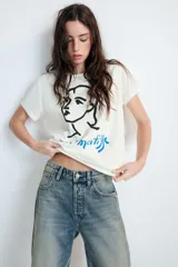 Remera de algodón de corte regular con cuello redondo y manga corta. Presenta un estampado frontal con un dibujo lineal de un rostro y la firma de Henri Matisse en color azul.