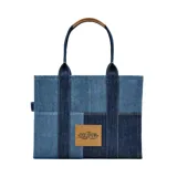 Bolso tipo tote de Marc Jacobs confeccionado en denim azul con diseño de paneles en diferentes tonos. Presenta el logo 'THE TOTE BAG' estampado en la parte frontal y doble asa superior.