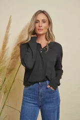 Buzo negro de punto con cuello polo y cierre parcial de botones dorados en forma de trébol.