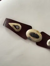 Cinto tipo faja de cuero color marrón chocolate, con apliques metálicos grabados de formas geométricas y piedras oscuras incrustadas.