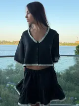 Top de lino con silueta relajada, escote en V y cierre frontal con botones. Presenta detalles de puntilla blanca en el escote, ruedo y mangas.