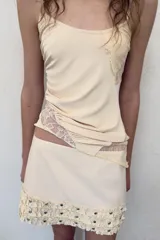Falda mini de tiro medio en color crudo, con detalle de volantes y tachas metálicas en el ruedo. Cuenta con cierre lateral con cremallera oculta.