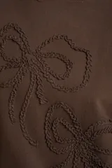 Sweater marrón de algodón con cuello redondo y diseño de moños en relieve bordados en el frente.
