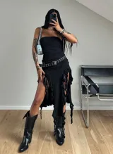 Vestido midi negro sin tirantes, de corte tubo con fruncido frontal y falda asimétrica con aberturas laterales, volados y detalles de tiras colgantes.
